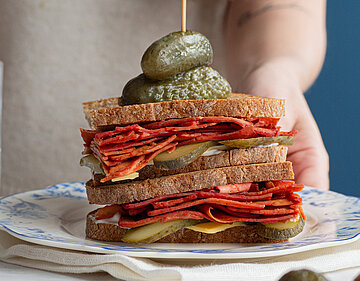 Sandvich mit dünnen Tofuscheiben, Käse und Gurken auf einem Teller mit Dekoration.