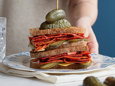 Sandvich mit dünnen Tofuscheiben, Käse und Gurken auf einem Teller mit Dekoration.