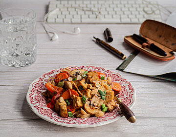 Tofuwürfel an Tofuwürfel mit buntem Gemüse und Erdnüssen auf einem Teller, der vor einer Tastatur steht mit Dekoration.