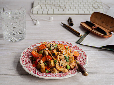 Tofuwürfel an Tofuwürfel mit buntem Gemüse und Erdnüssen auf einem Teller, der vor einer Tastatur steht mit Dekoration.