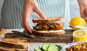 Zwischen 2 Graubrotscheiben Tofu-Stückchen und Salat auf einem Holzbrett und Dekoration.