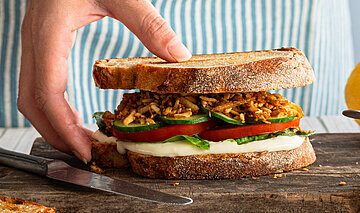 Zwischen 2 Graubrotscheiben Tofu-Stückchen und Salat auf einem Holzbrett und Dekoration.